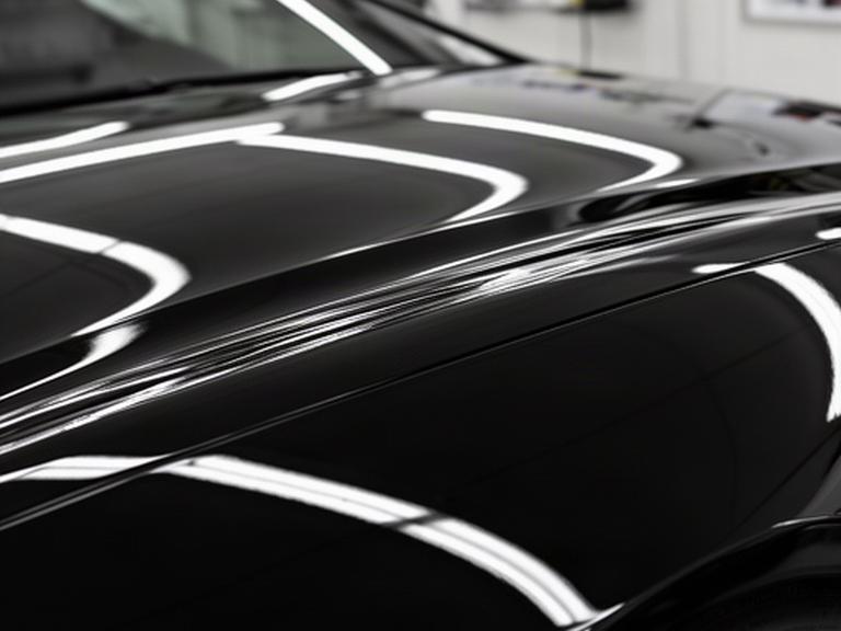 Black performance car bonnet after machine paint correction with sharp reflected lights